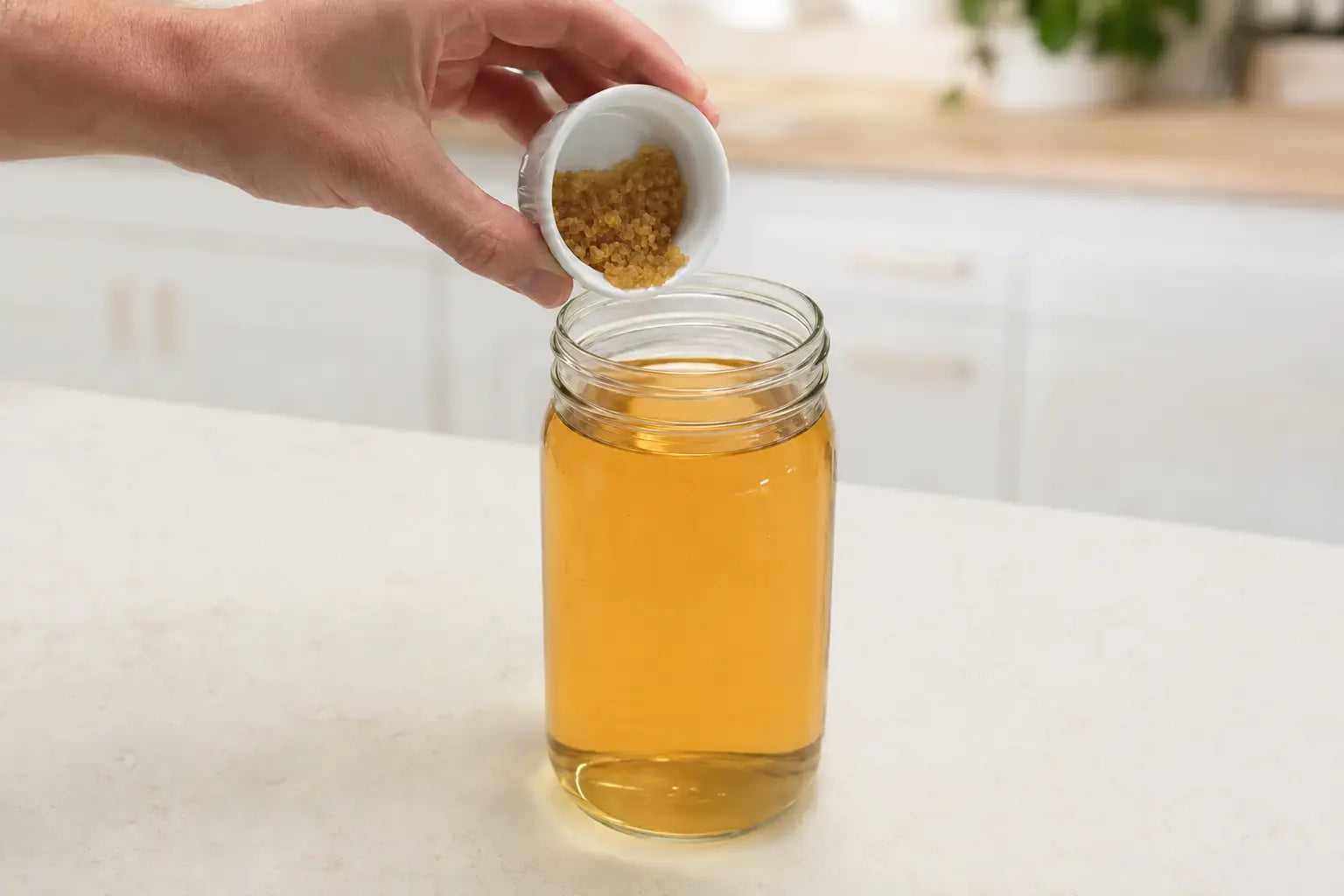 Dehydrated water kefir grains being added to an amber jar of prepared sugar water